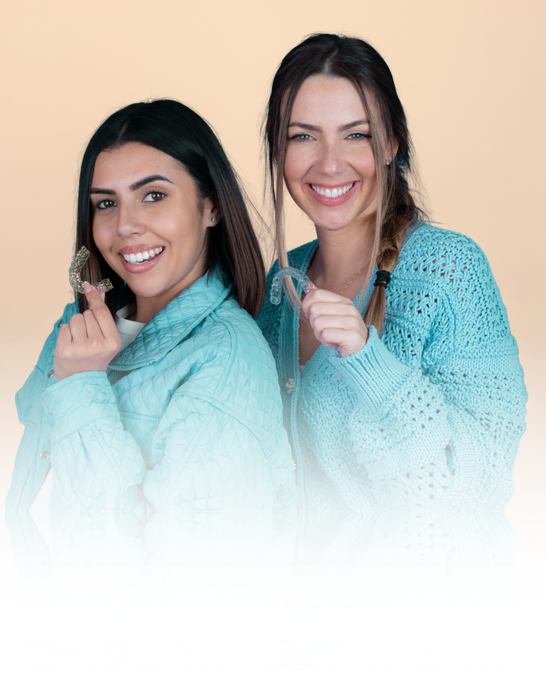 Two people smiling and holding clear aligners